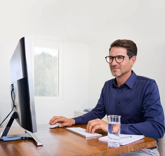 Mann mit Arbeitsplatzbrille sitzt am Schreibtisch und schaut in einen Bildschirm.